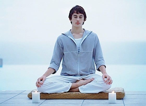 A man in lotus posture meditating on a dock.