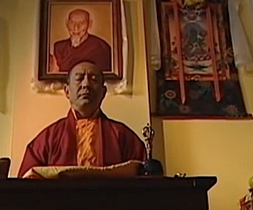 A still frame from the movie "Come Again" featuring Zasep Rinpoche. Behind him is a portrait of his guru H.H. Zong Rinpoche.