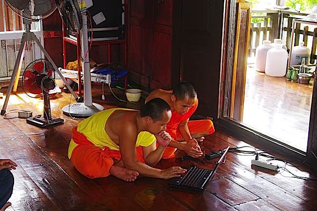 Buddhist monks in Thailand using a computer on the floor of the temple. Computers, mobile phones and tablets are common today in temples and monasteries.