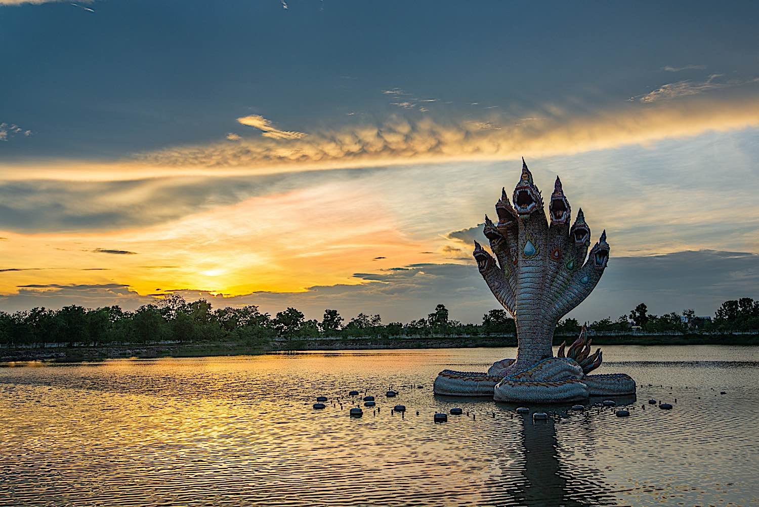 Beautiful Naga statue at sunset, rising up out of the water, in Wat Ban Rai Buddhist Temple Nakhonratchasima Thailand.