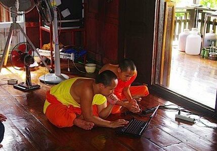 Buddhist monks in Thailand using a computer on the floor of the temple. Computers, mobile phones and tablets are common today in temples and monasteries.