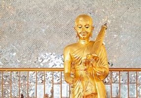 Gold Phra Sivali Bhante Statue. His famous attributes are he is walking, with an walking stick, begging bowl, beads and and umbrella on one shoulder.
